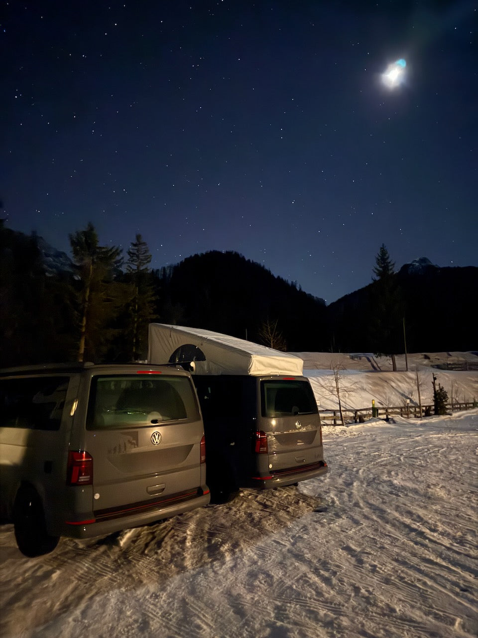 Zwei VW California Camper nachts im Schnee mit aufgebautem Dach und Sternenhimmel